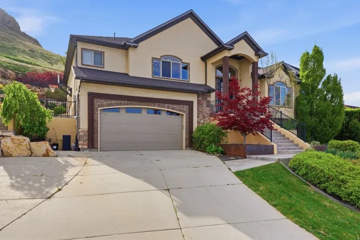 View of front facade featuring stone siding, driveway, stucco siding, and a garage