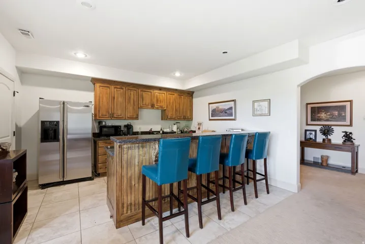 Lower level kitchen featuring wood cabinetry, a breakfast bar area, fridge, light tile floors