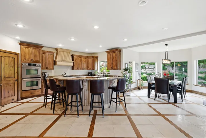 Kitchen with inlaid floor details, a breakfast bar, light stone counters, stainless steel double oven, and wood finish cabinets