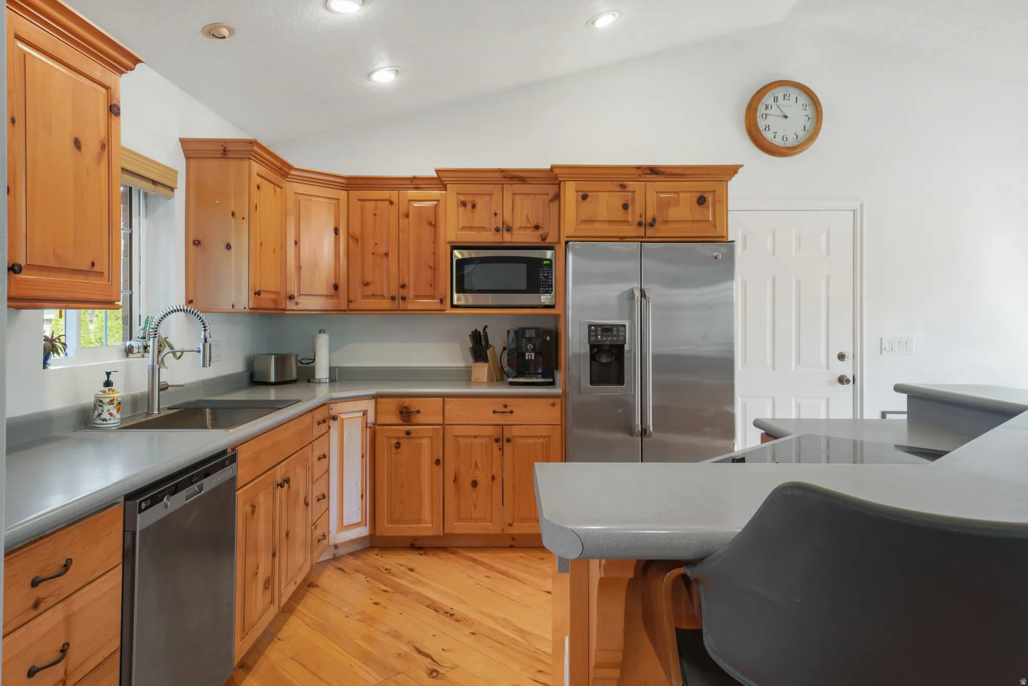 Kitchen featuring stainless steel appliances, light wood-style flooring, light countertops, lofted ceiling, and a breakfast bar