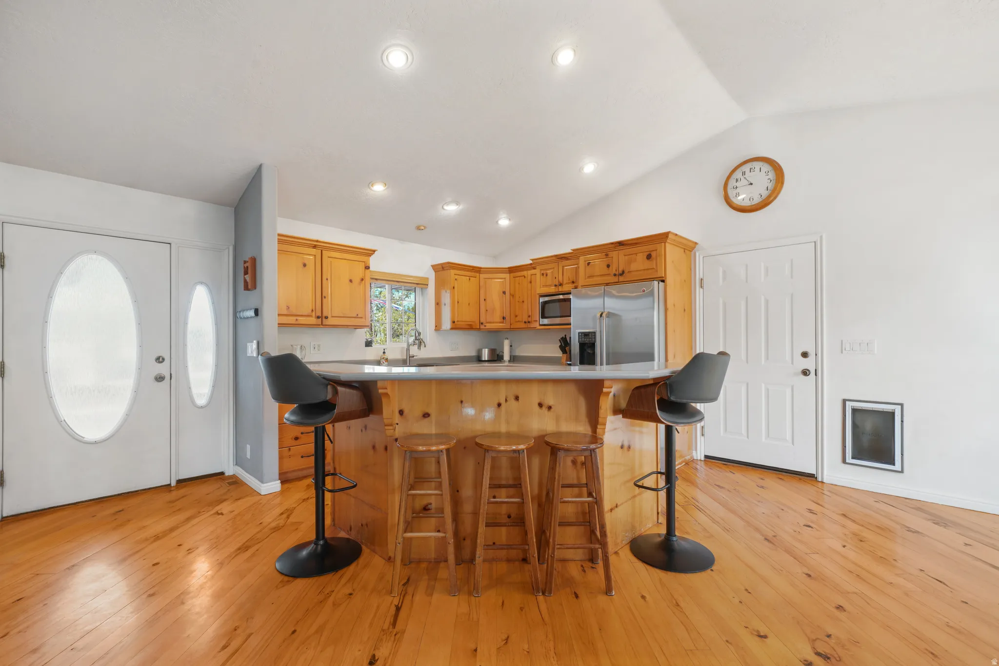 Kitchen featuring stainless steel appliances, light wood finished floors, a center island, lofted ceiling, and a kitchen bar