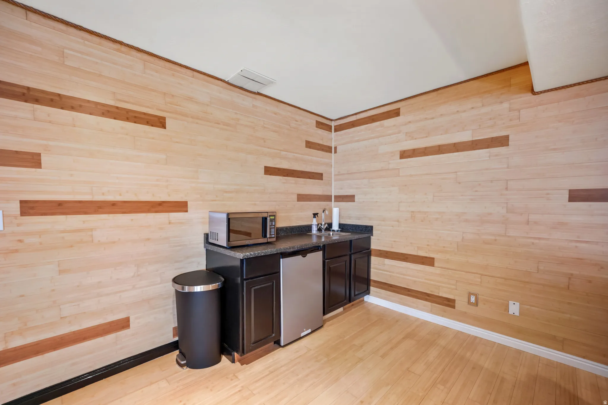 Bar with dark countertops, wood walls, light wood-type flooring, and stainless steel appliances