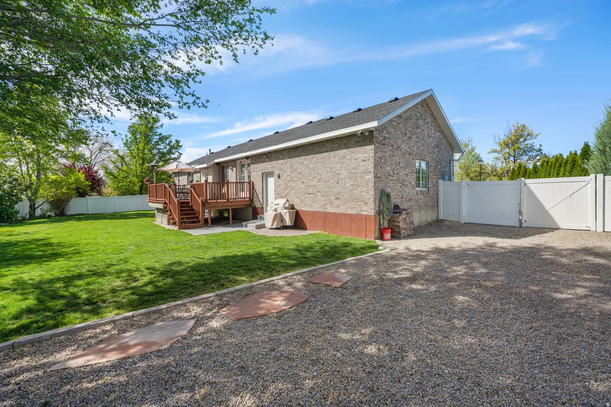 Rear view of house with a gate, a fenced backyard, a wooden deck, brick siding, and a patio area