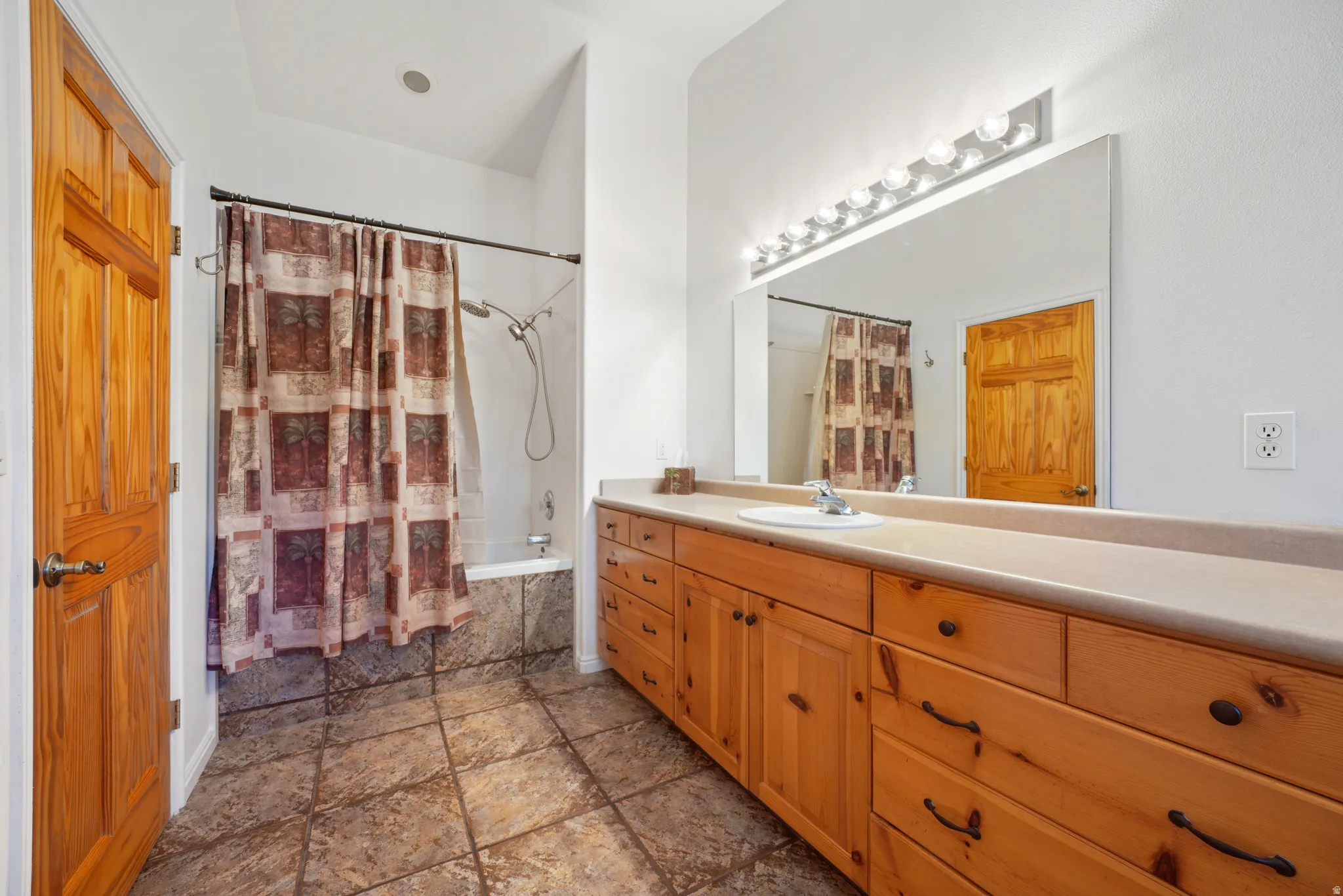 Master Bathroom with tiled shower / bath, vanity, and dark stone finish flooring