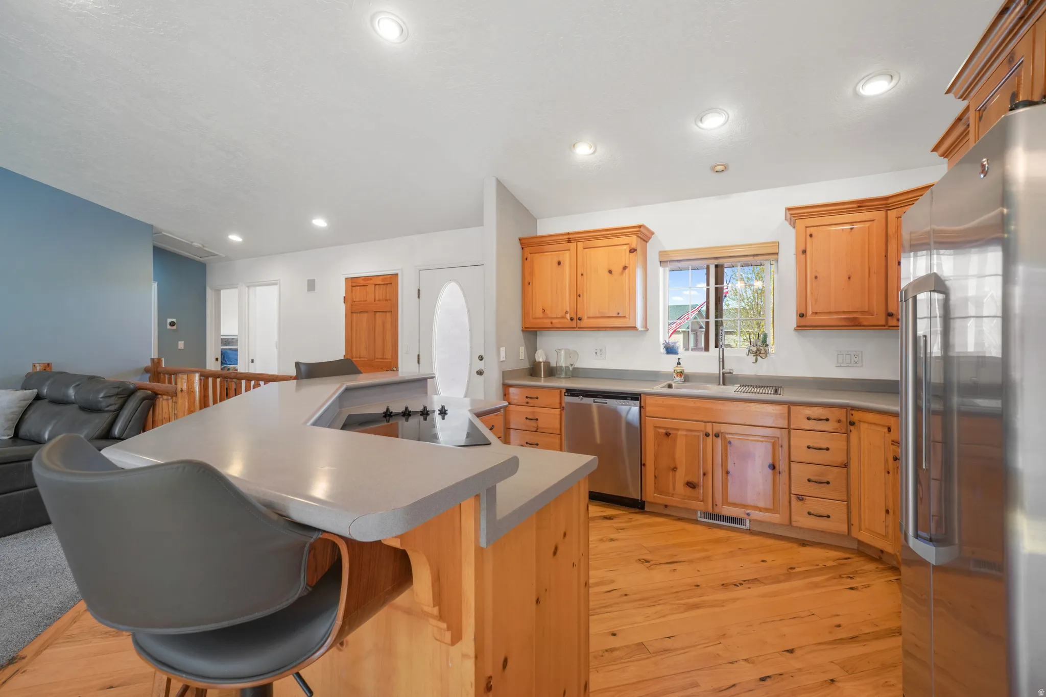 Kitchen with stainless steel appliances, light wood-type flooring, a kitchen island with sink, recessed lighting, and light countertops