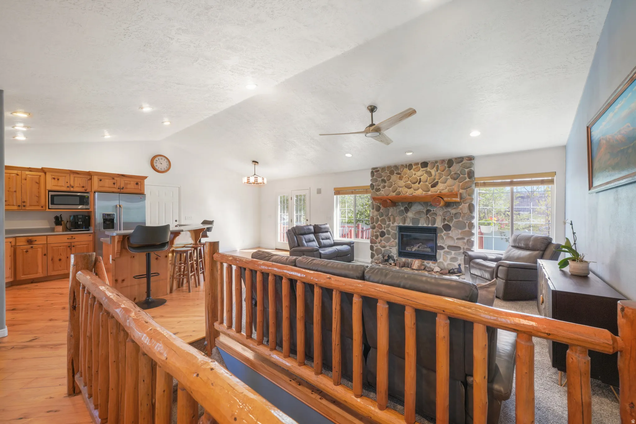Living area featuring a ceiling fan, light wood-style floors, and a stone fireplace