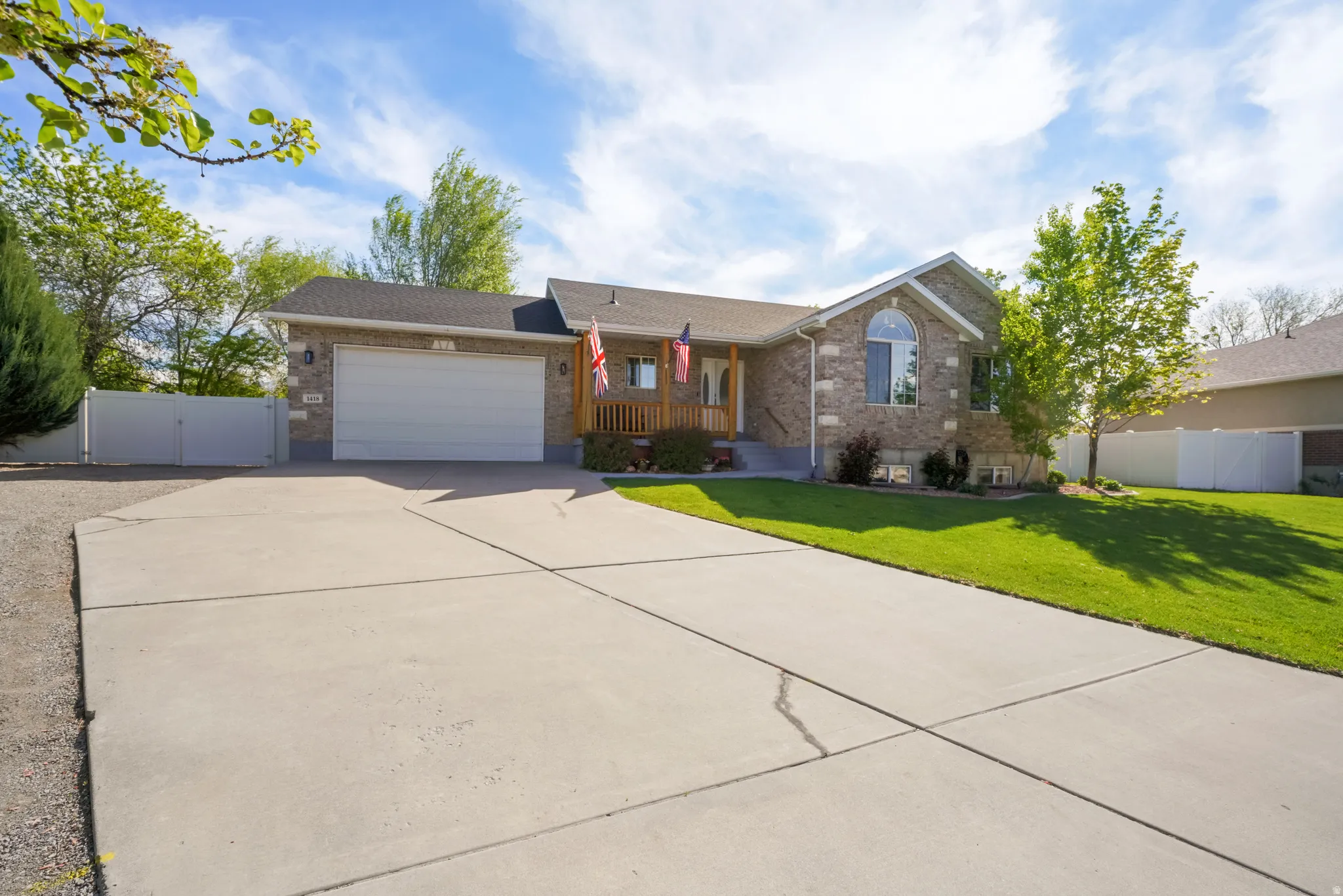Ranch-style house featuring a porch, an attached garage, driveway, brick siding, and a gate
