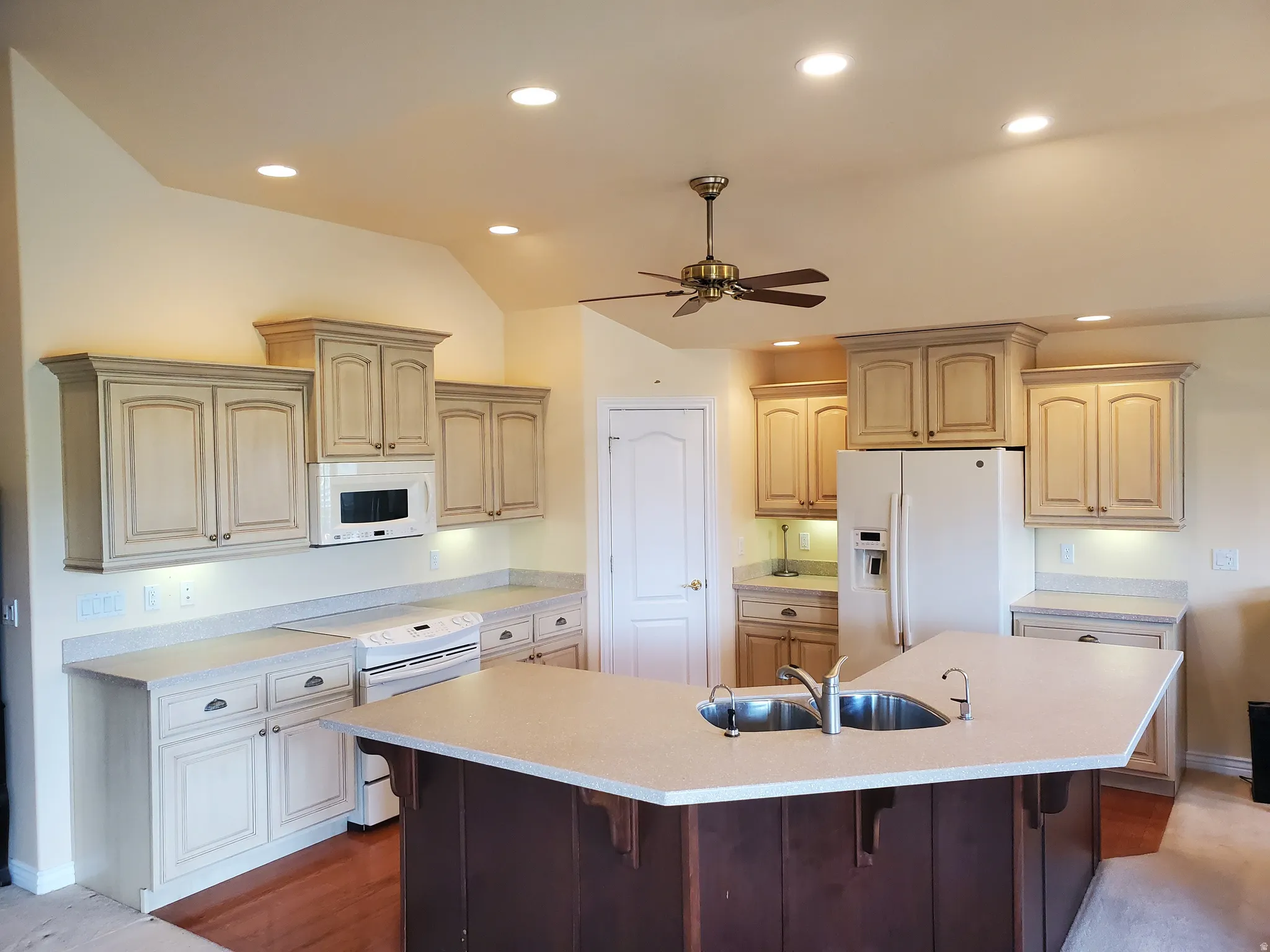 Kitchen with white appliances, a kitchen bar, a ceiling fan, a large island with sink, and recessed lighting