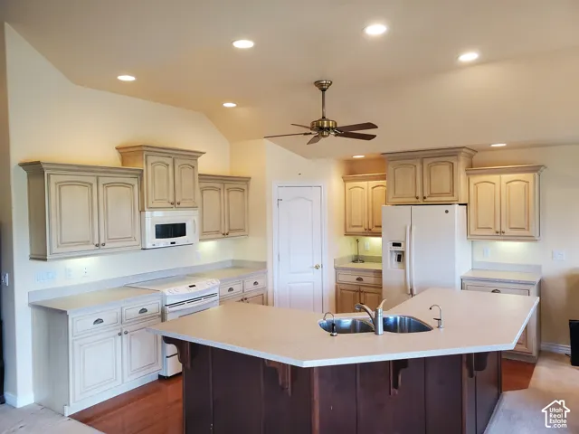 Kitchen with white appliances, a kitchen bar, a ceiling fan, a large island with sink, and recessed lighting