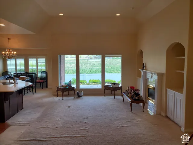 Living room with light colored carpet, a high end fireplace, a chandelier, plenty of natural light, and vaulted ceiling
