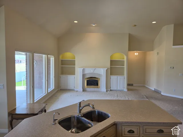 Vaulted ceilings, built-in shelving, fireplace with decorative mantel, dual basin sink, and recessed lighting
