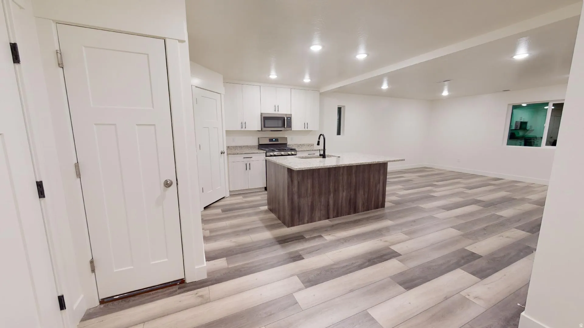 Kitchen featuring light wood-style floors, a center island with sink, light stone countertops, stainless steel appliances, and two tone color scheme