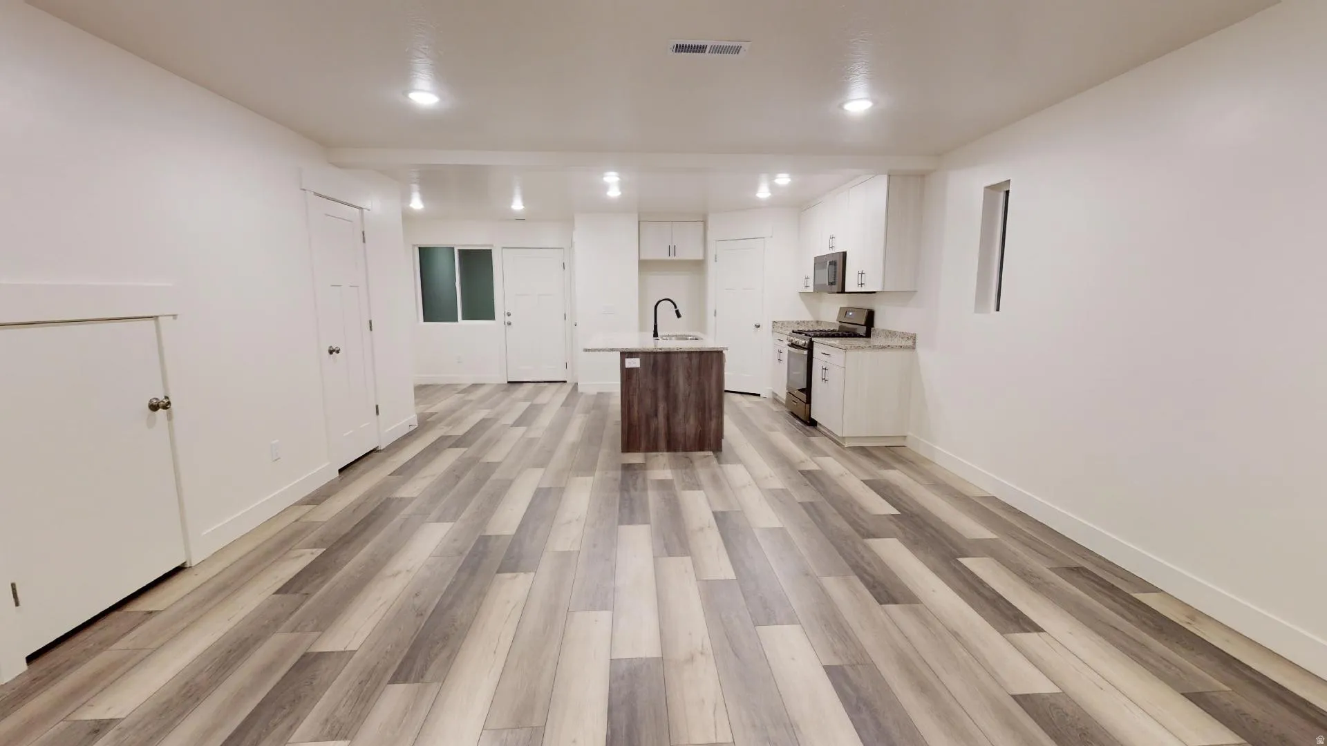 Dual tone kitchen featuring stainless steel appliances, a center island with sink, two tone cabinets, light wood-style flooring, and open floor plan