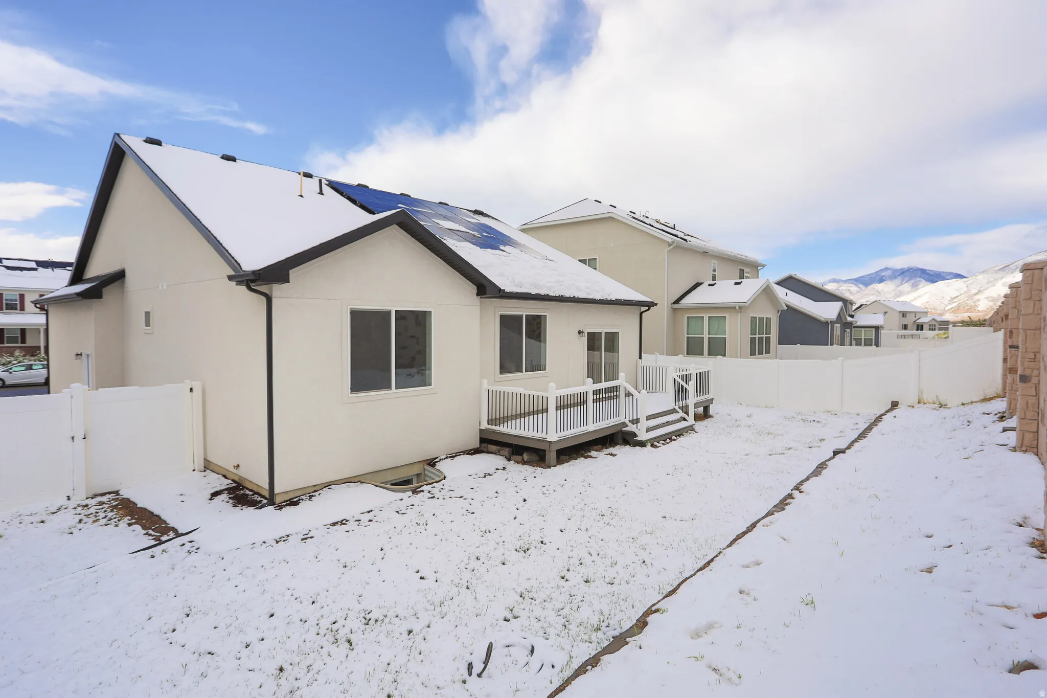 Snow covered property featuring a fenced backyard, a deck with mountain view, stucco siding, and a gate