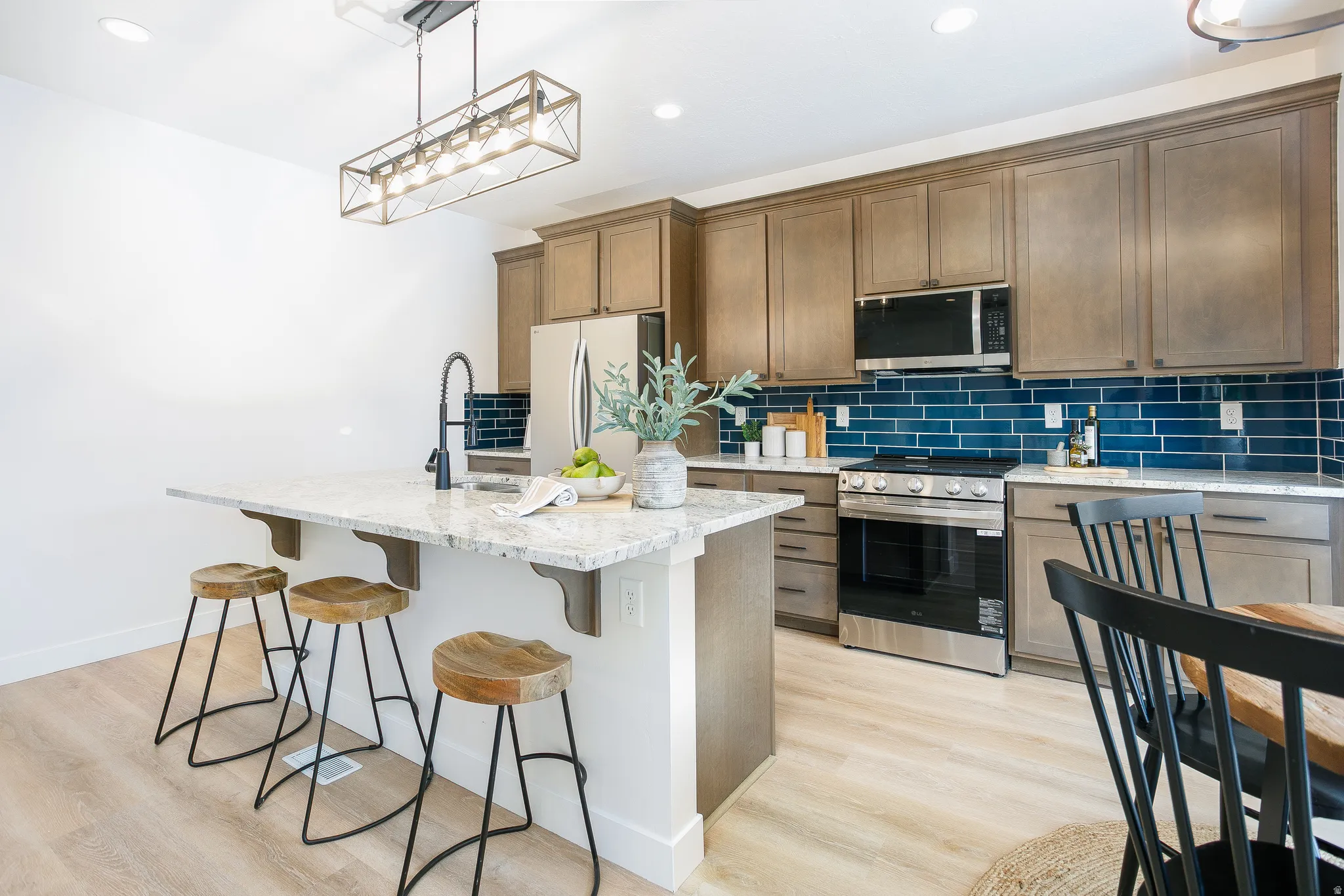 Kitchen featuring a breakfast bar, stainless steel appliances, light wood finished floors, a center island with sink, and light stone counters