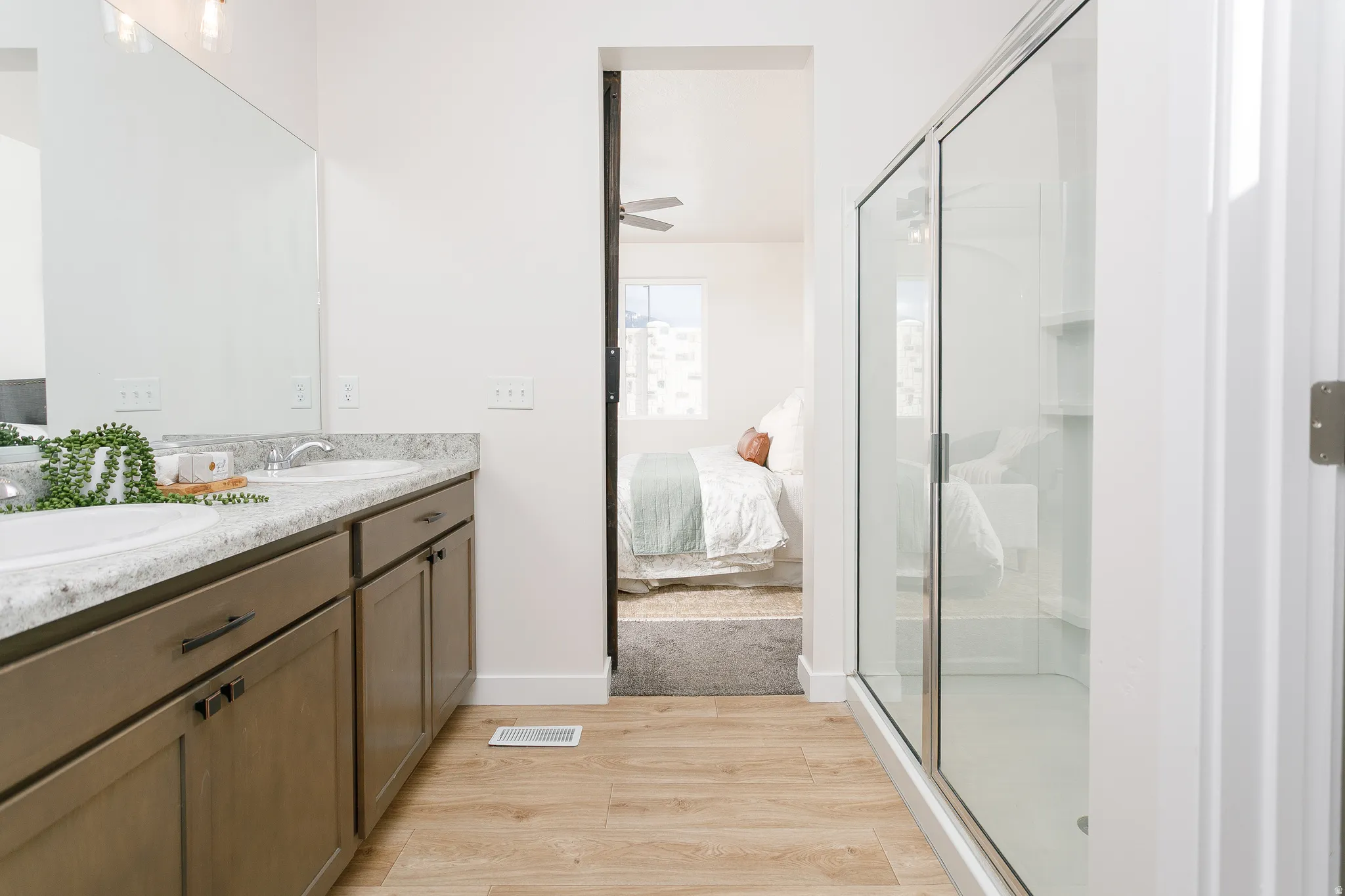 Full bathroom featuring connected bathroom, light wood-style flooring, double vanity, and a shower stall