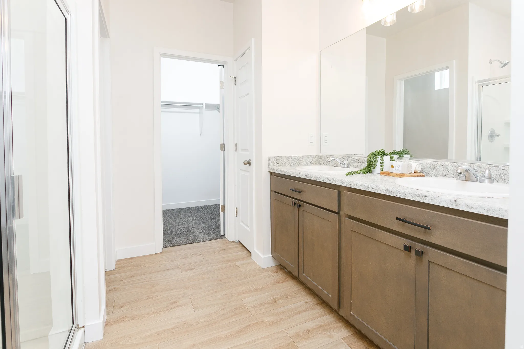 Full bathroom with a stall shower, double vanity, light wood finished floors, and a walk in closet