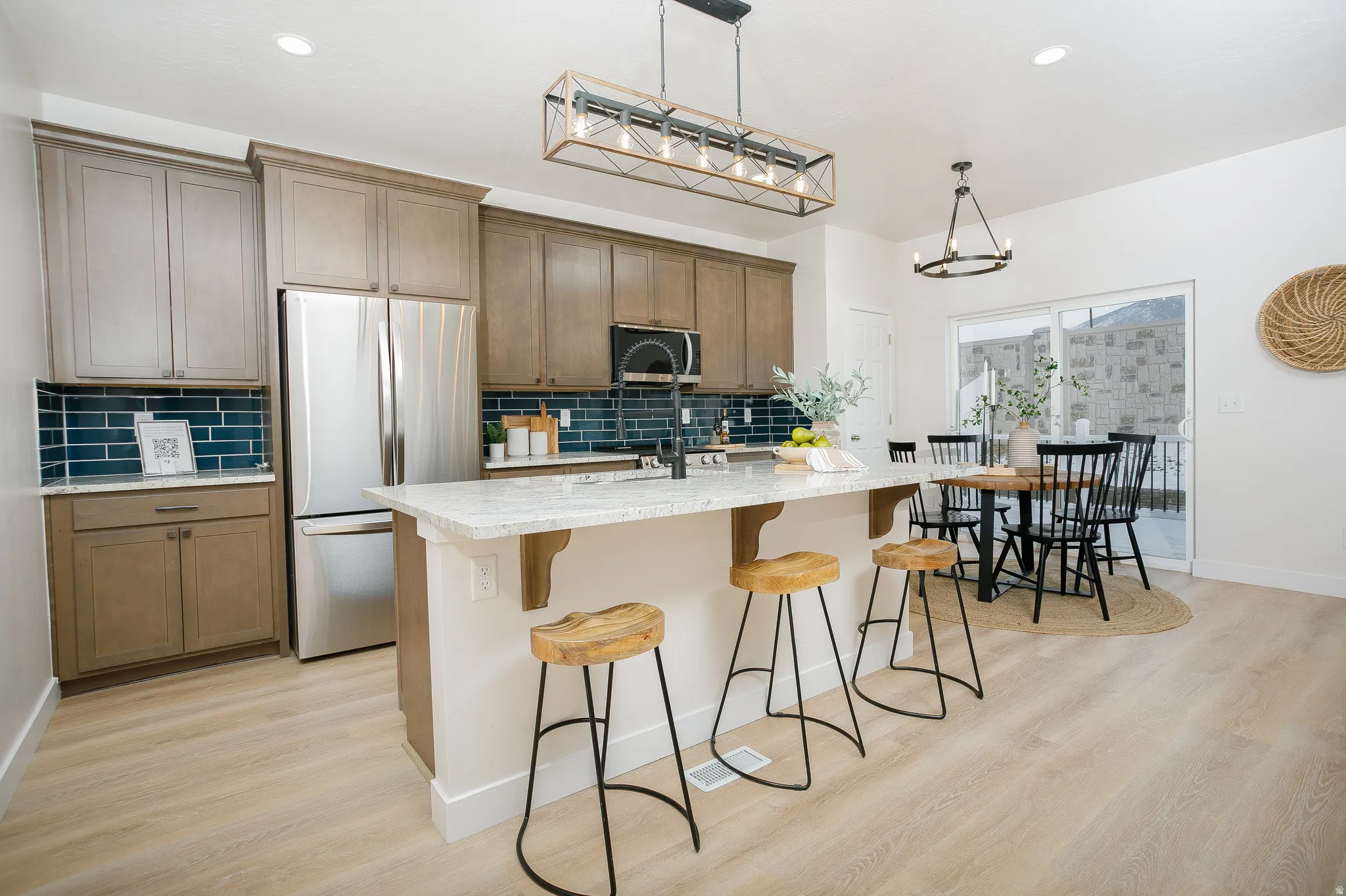 Kitchen with freestanding refrigerator, a center island with sink, light wood-style flooring, a breakfast bar area, and light stone countertops