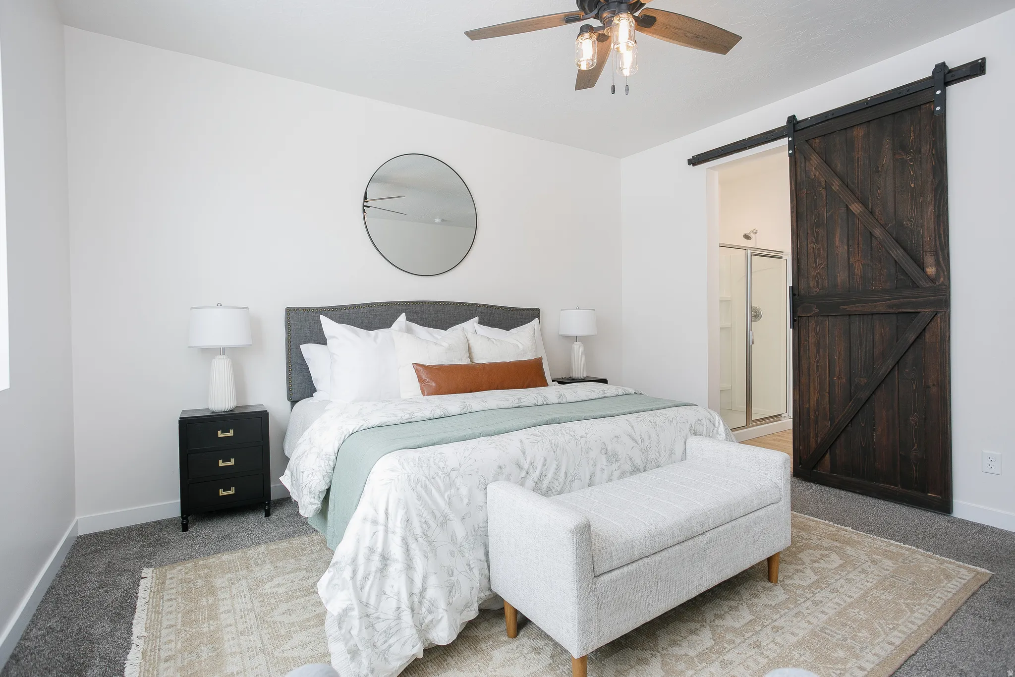 Carpeted bedroom with a barn door, ensuite bath, and a ceiling fan