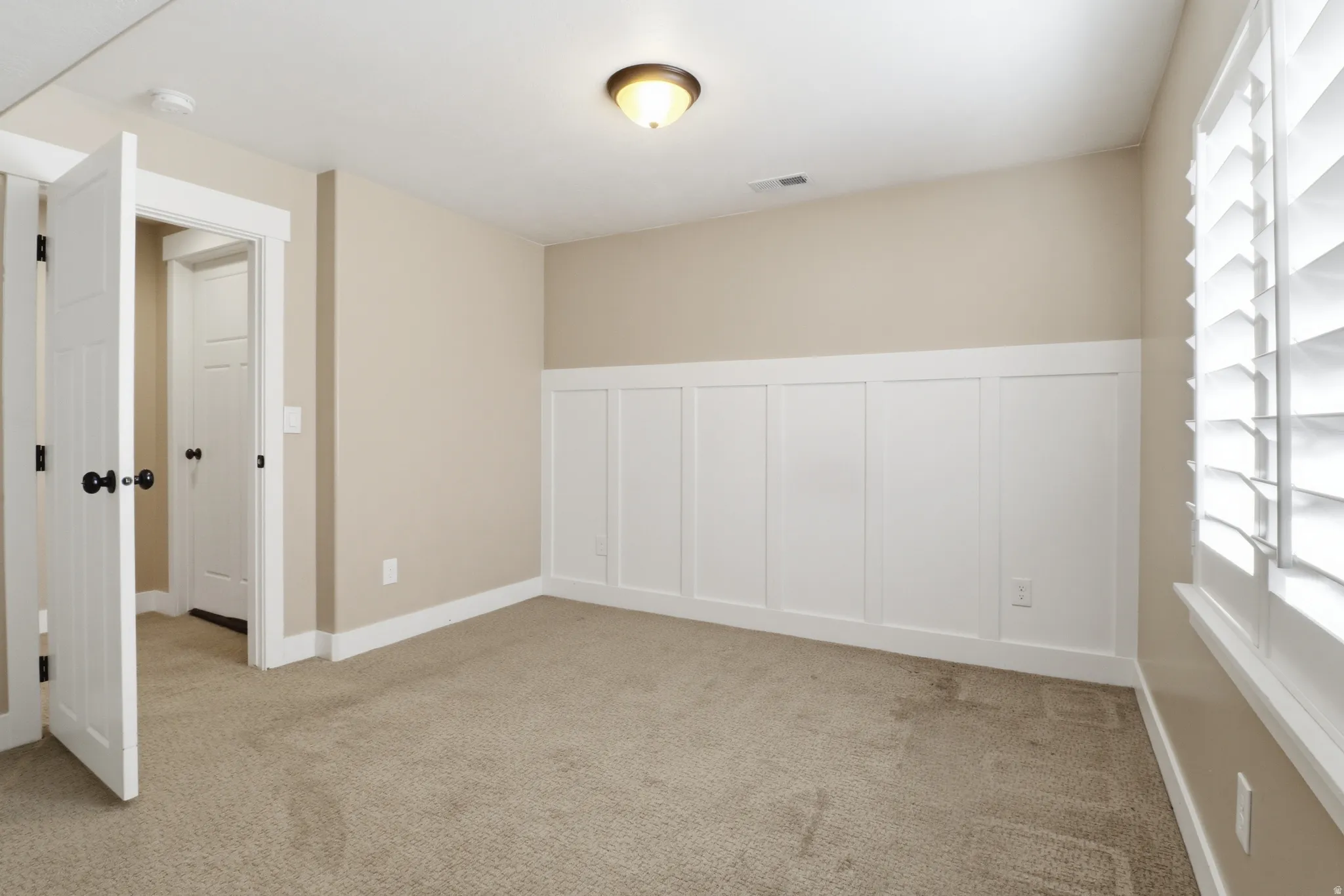 Unfurnished room featuring light colored carpet, wainscoting, and a decorative wall