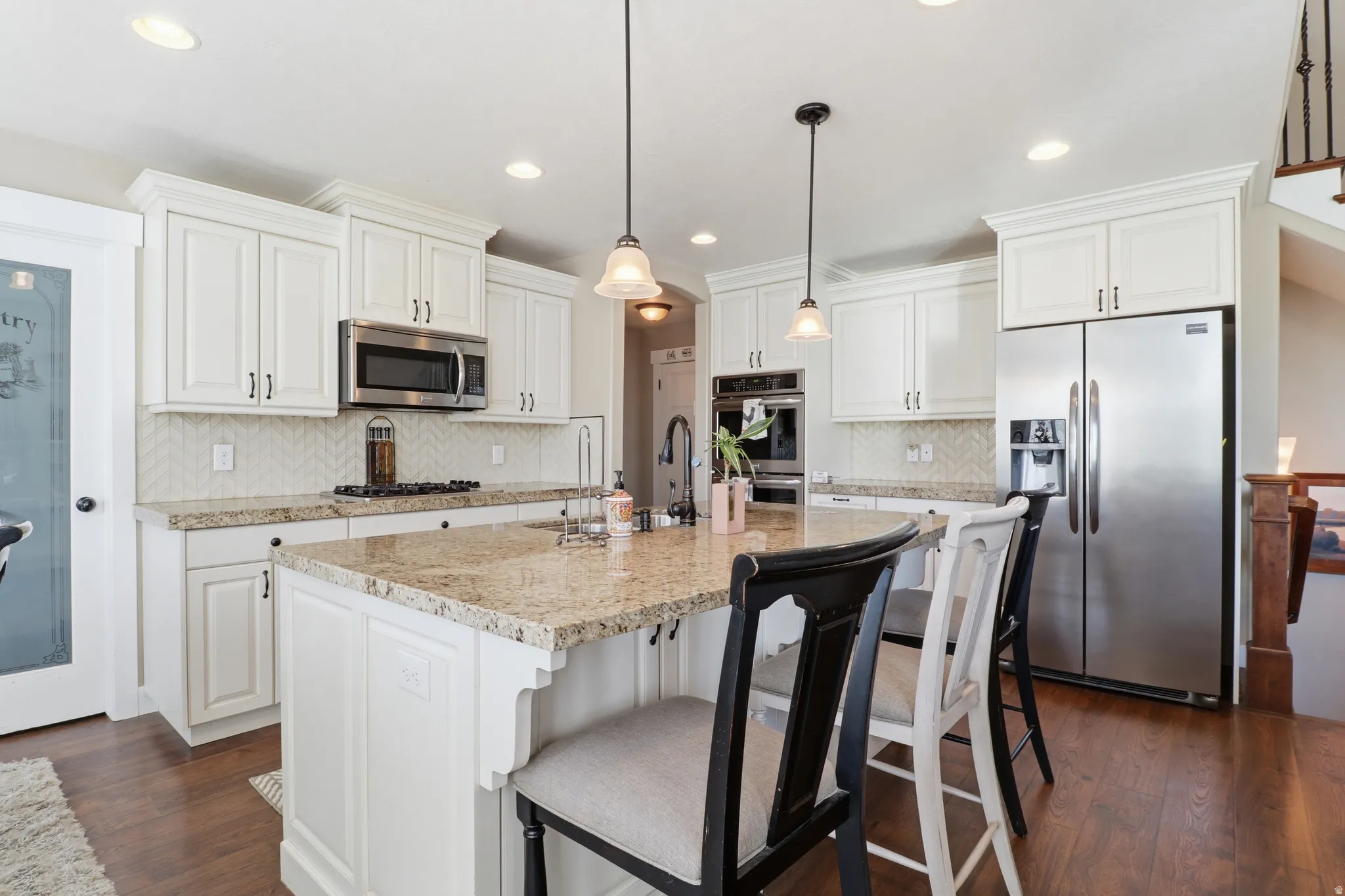 Kitchen with stainless steel appliances, a breakfast bar area, white cabinets, a kitchen island with sink, and dark wood-type flooring