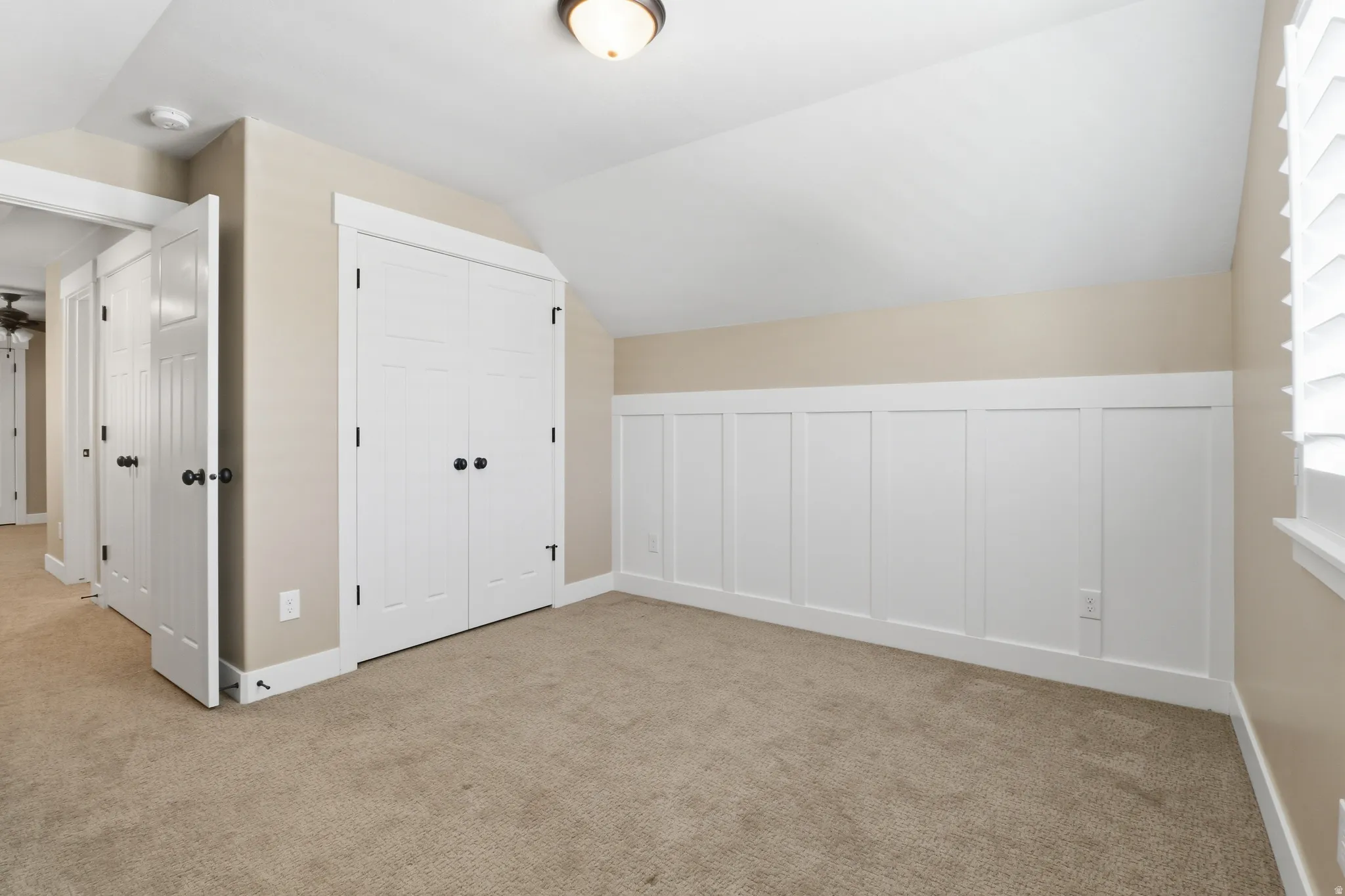 Bedroom featuring lofted ceiling, light carpet, wainscoting, and a decorative wall