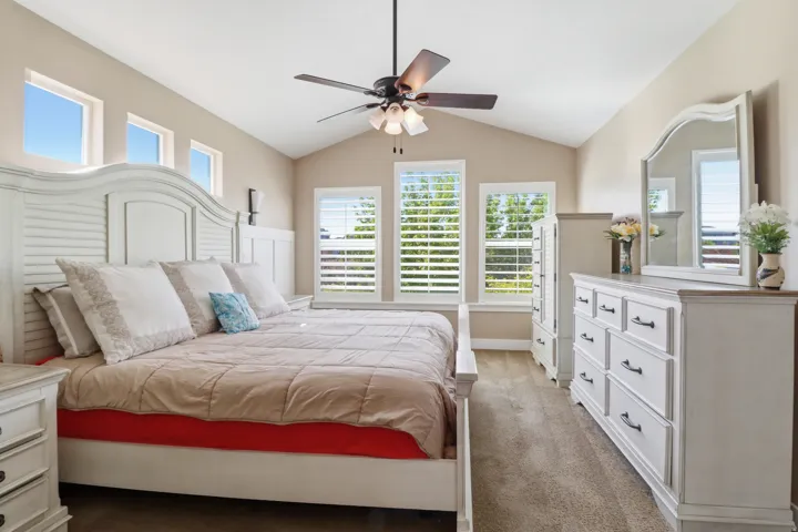 Carpeted master bedroom with lofted ceiling and a ceiling fan