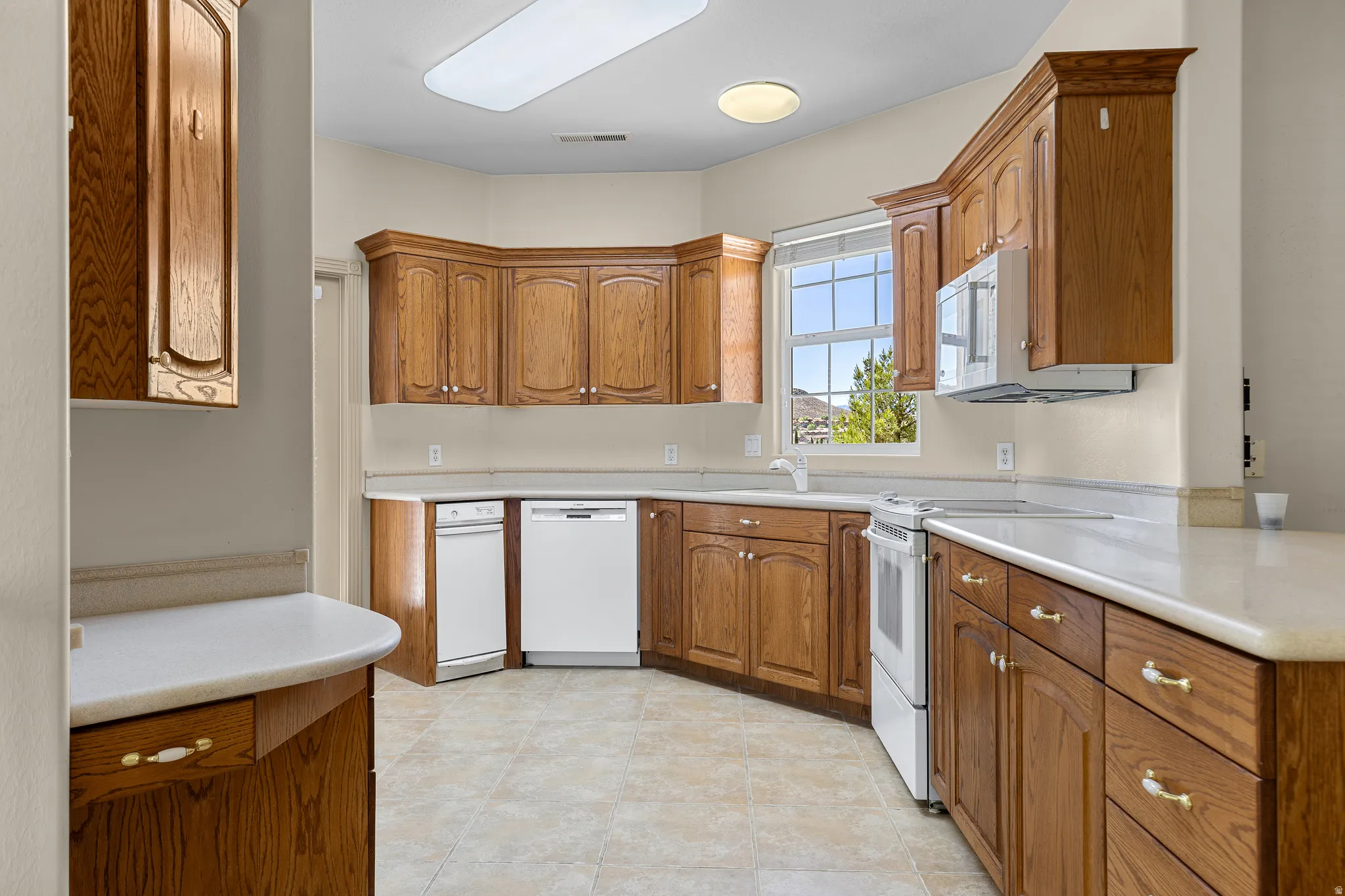 Kitchen with white appliances, light countertops, and wood finish cabinets