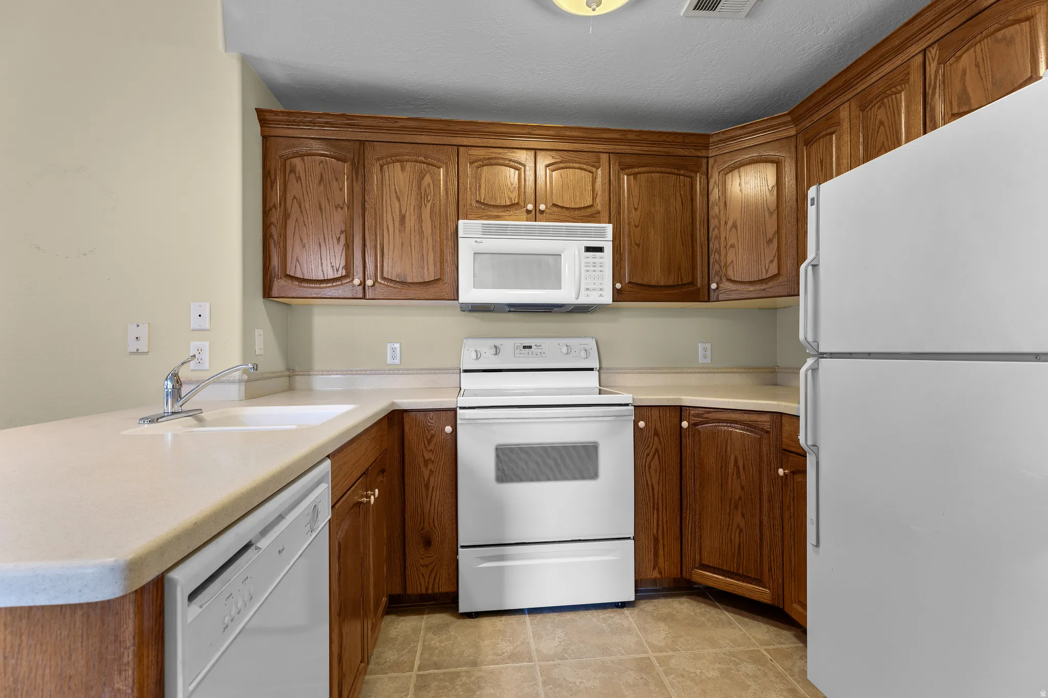Kitchen with white appliances, wood finish cabinetry, light countertops, and a peninsula