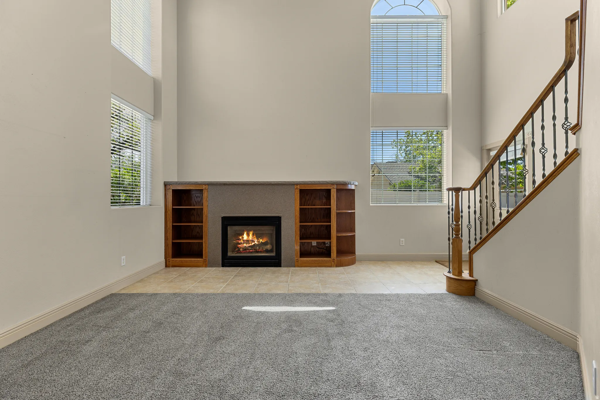 Unfurnished living room featuring a high ceiling, light colored carpet, a glass covered fireplace, and light tile patterned floors