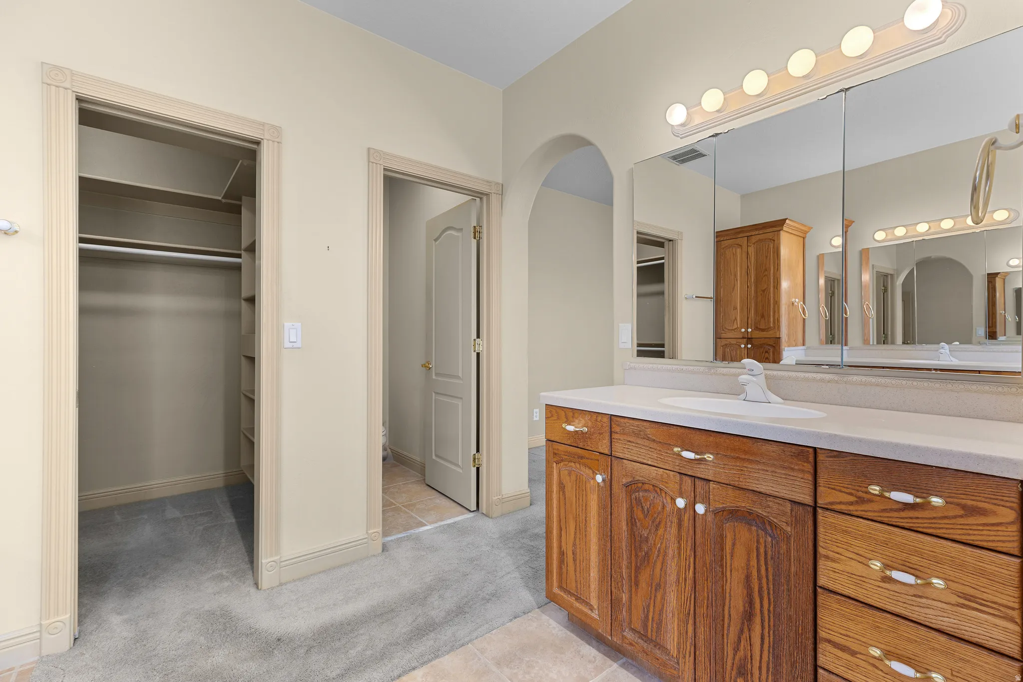 Bathroom with a spacious closet, vanity, light colored carpet, and light tile patterned floors