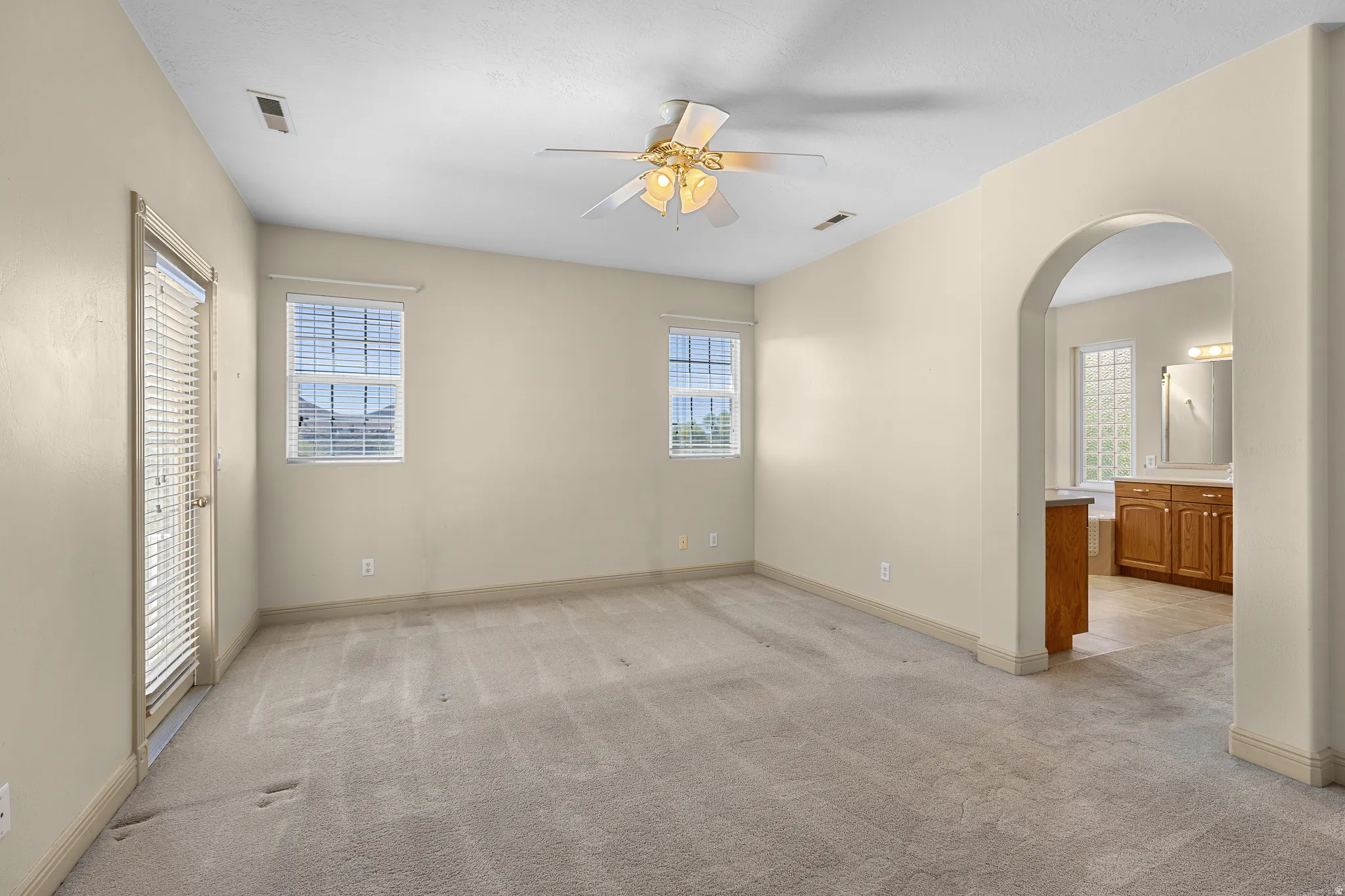 Unfurnished bedroom with arched walkways, multiple windows, and light colored carpet
