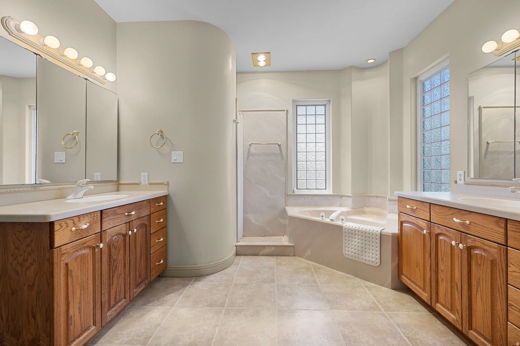 Bathroom featuring two vanities, a bath, a stall shower, and light tile patterned flooring
