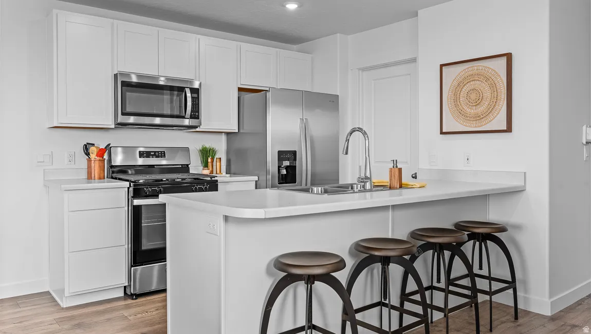 Kitchen with a breakfast bar area, a peninsula, stainless steel appliances, white cabinetry, and light countertops