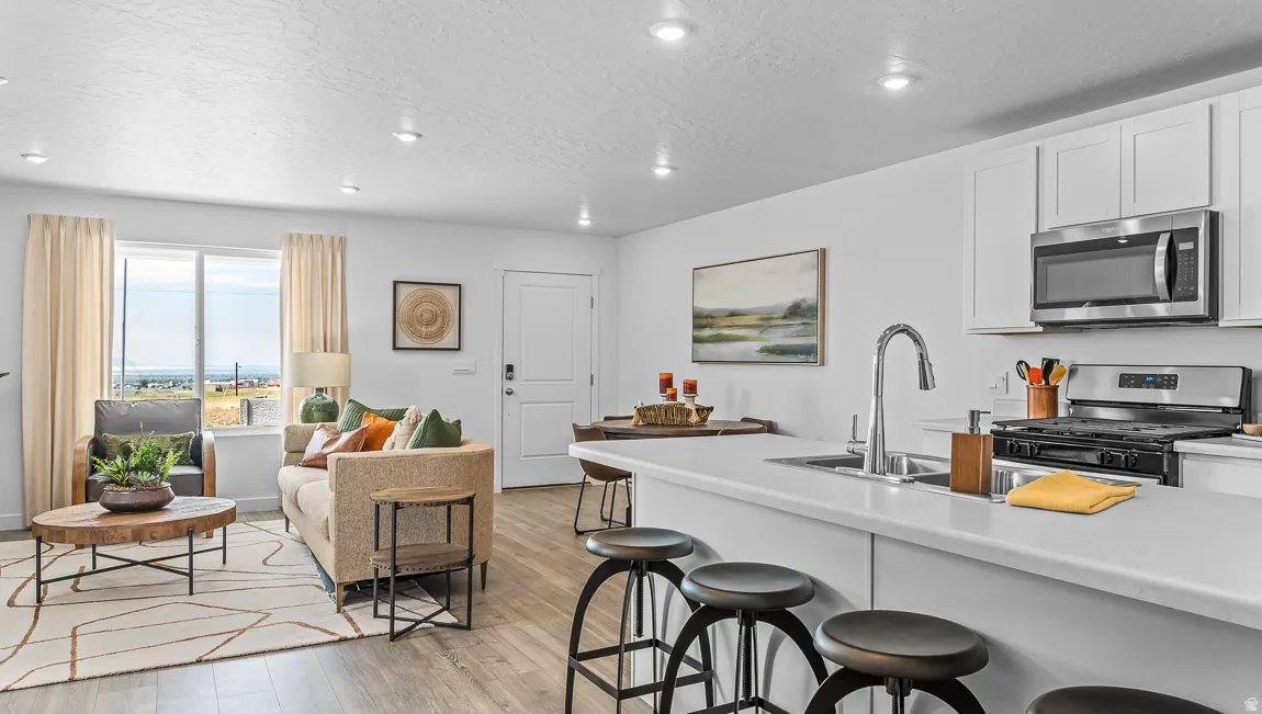 Kitchen featuring stainless steel appliances, light countertops, a breakfast bar area, white cabinetry, and light wood-type flooring