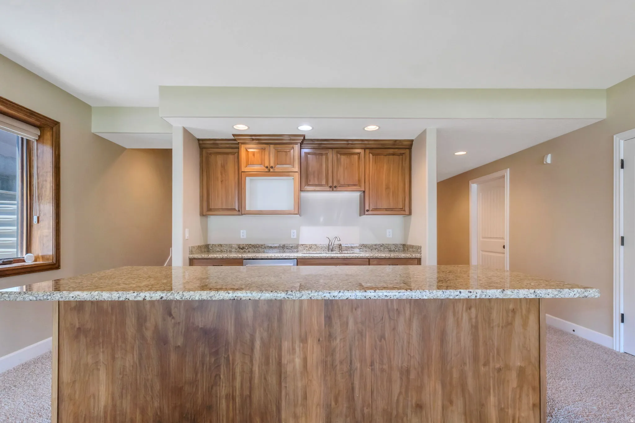 Bar area featuring a wood-finish peninsula with a granite-style countertop, recessed lighting, wood cabinetry, and an under-mount sink