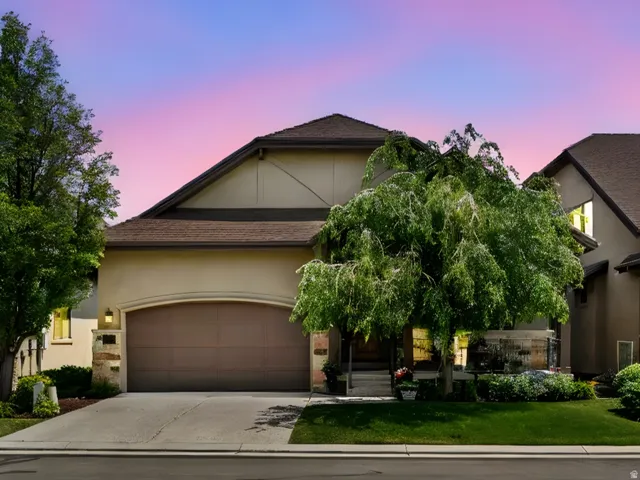 View of front of home featuring stucco siding, driveway, stone siding, and a front lawn