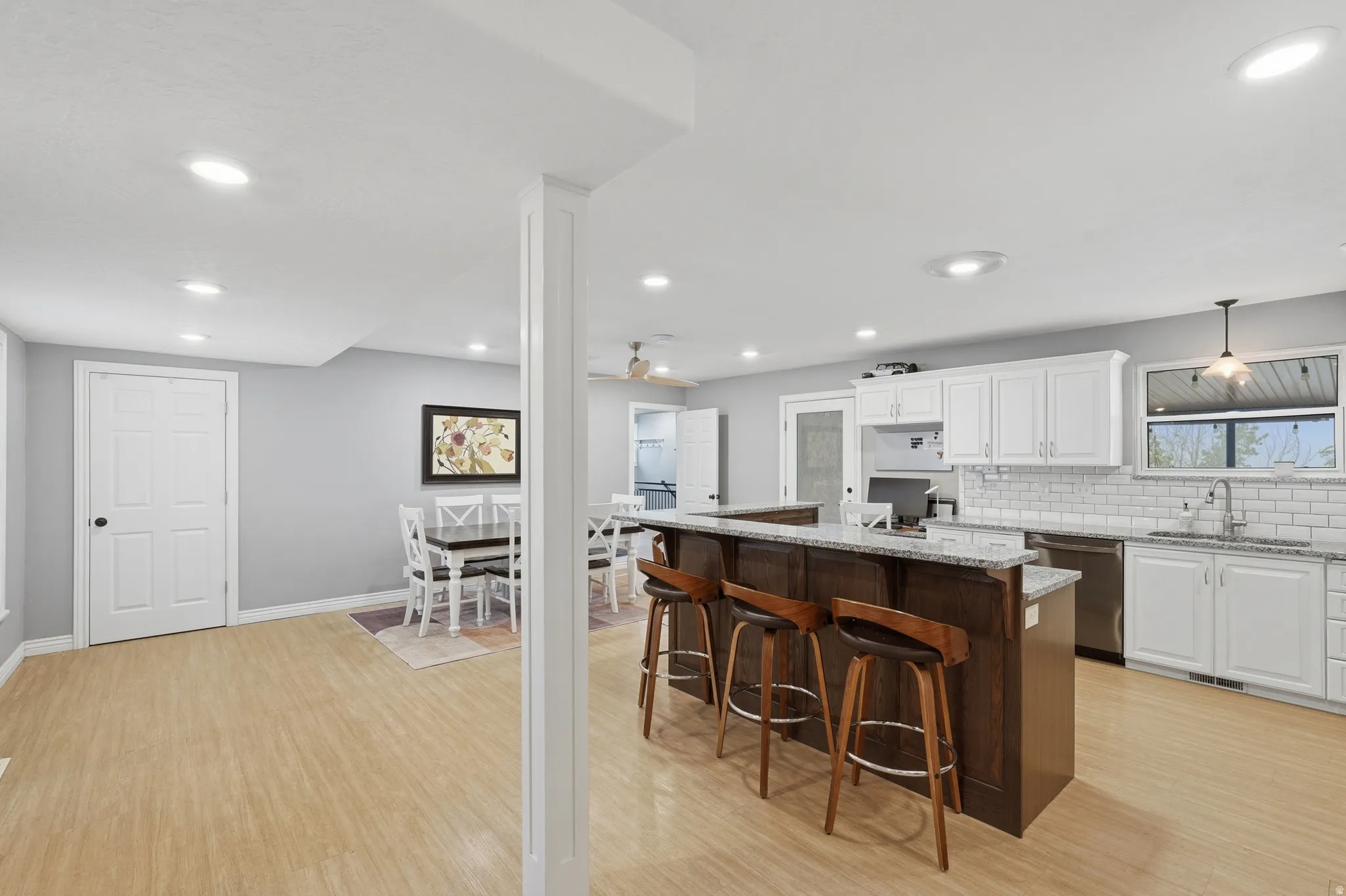 Dual tone kitchen with granite countertops, a kitchen bar, two tone cabinetry, a center island, and light wood-style flooring
