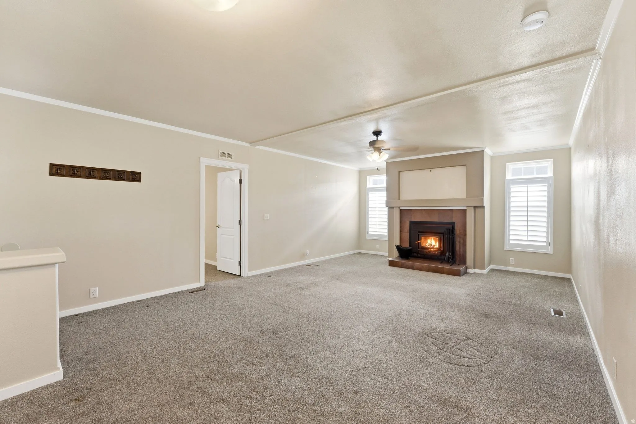 Unfurnished living room featuring a fireplace, ornamental molding, ceiling fan, and carpet flooring