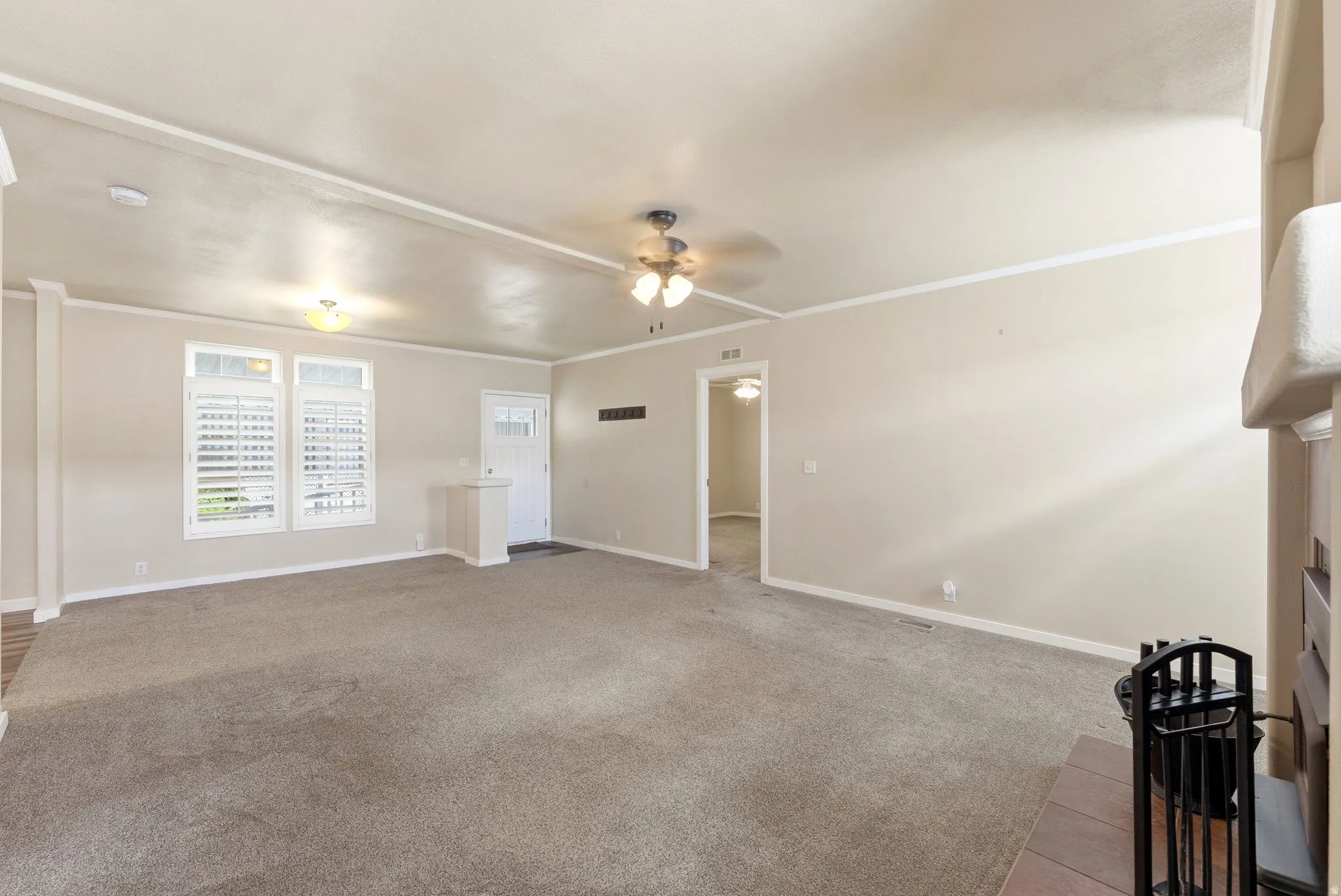 Unfurnished living room with ornamental molding, light carpet, a ceiling fan, and a fireplace