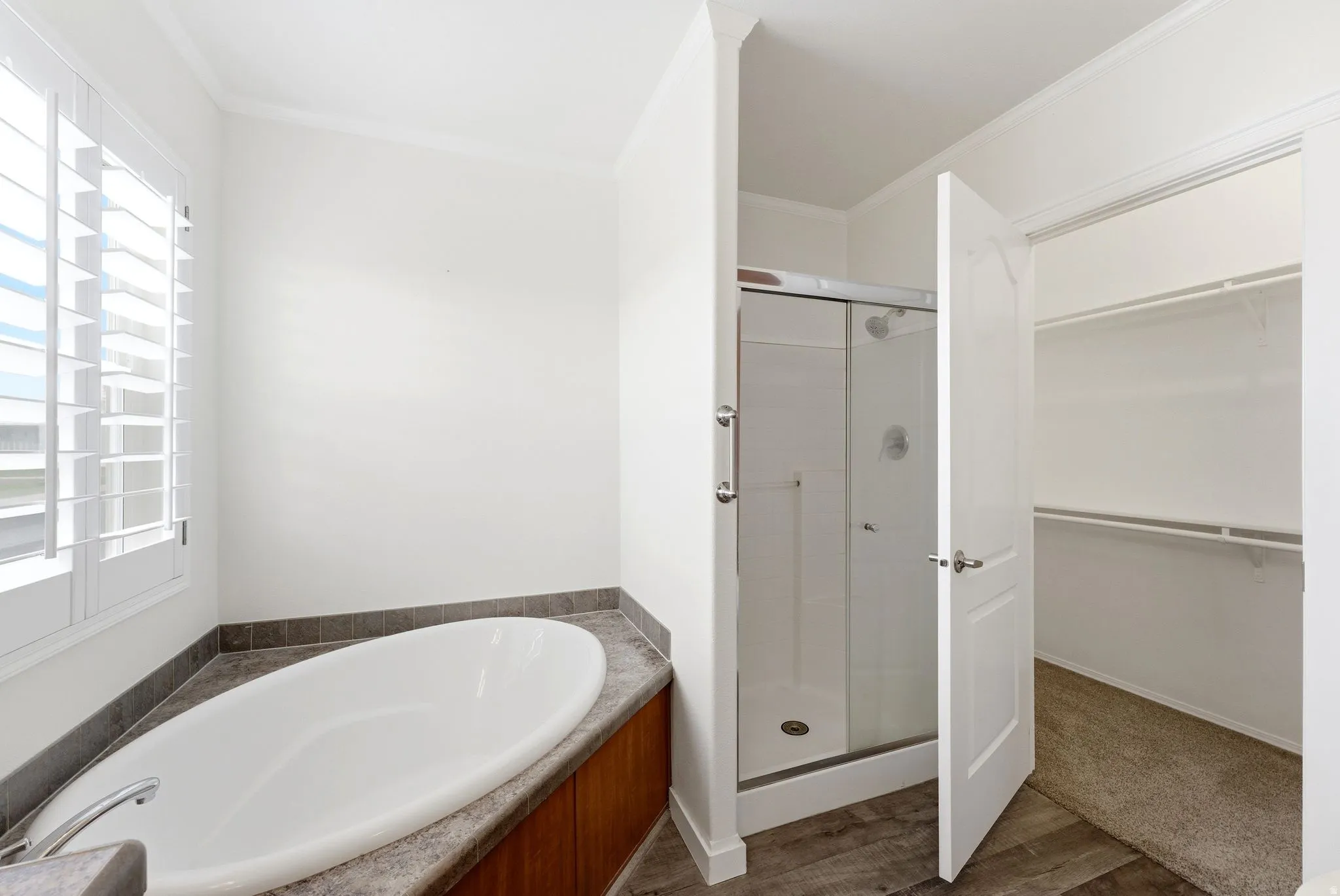 Full bath with a stall shower, a bath, a spacious closet, ornamental molding, and dark wood-type flooring