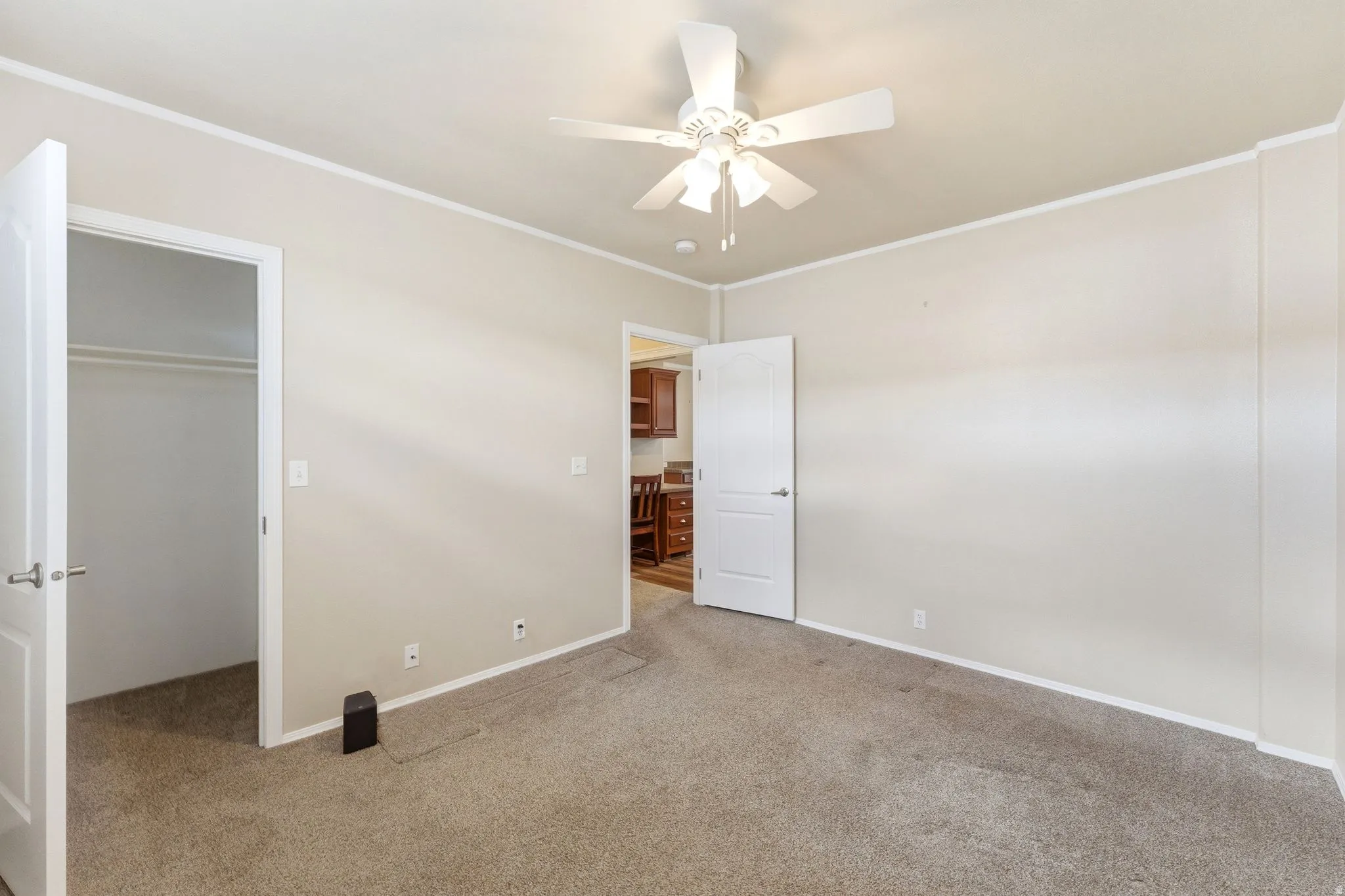 Unfurnished bedroom with crown molding, light colored carpet, a spacious closet, and ceiling fan