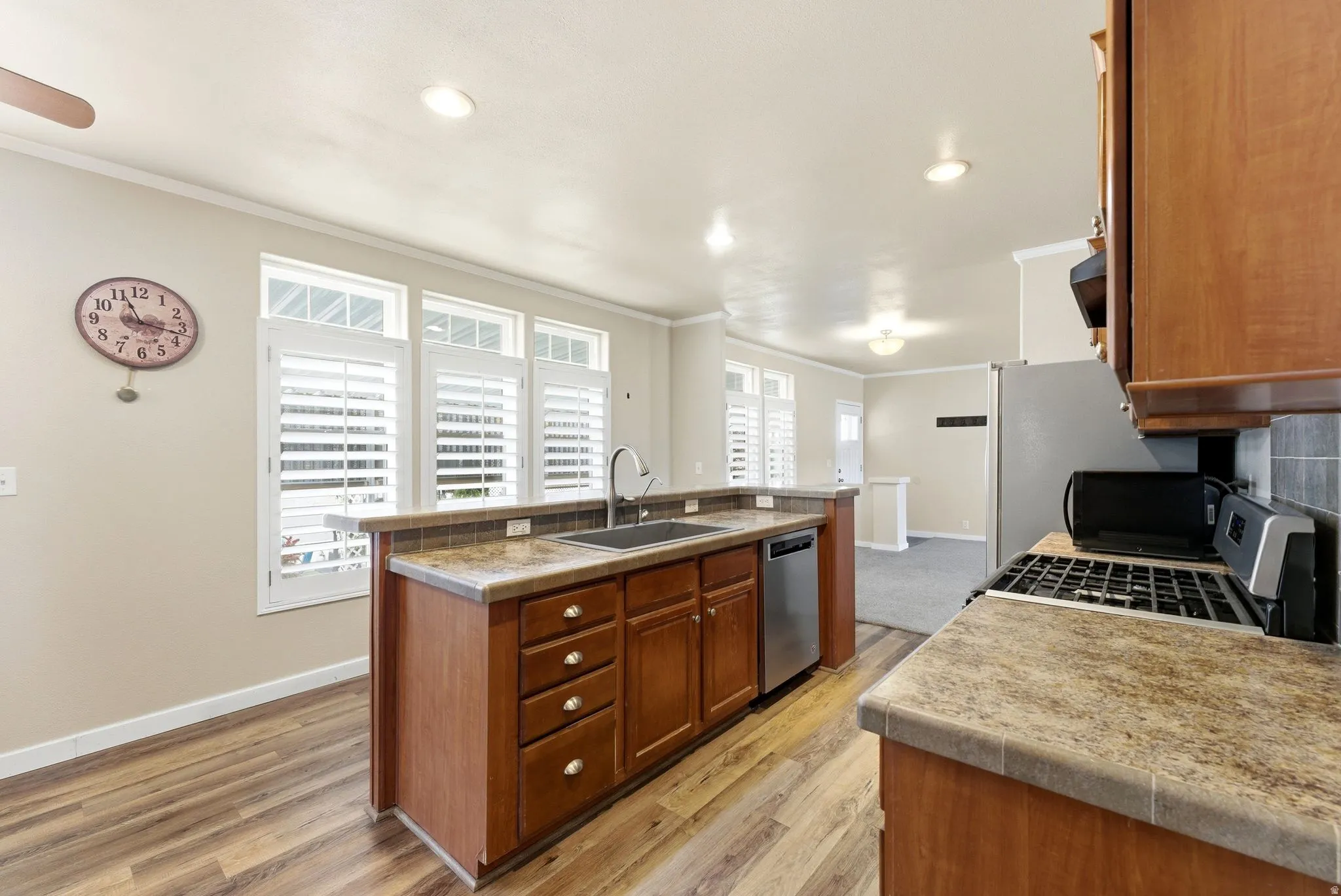 Kitchen with a kitchen island with sink, wood finish cabinetry, ornamental molding, light wood-style floors, and stainless steel appliances