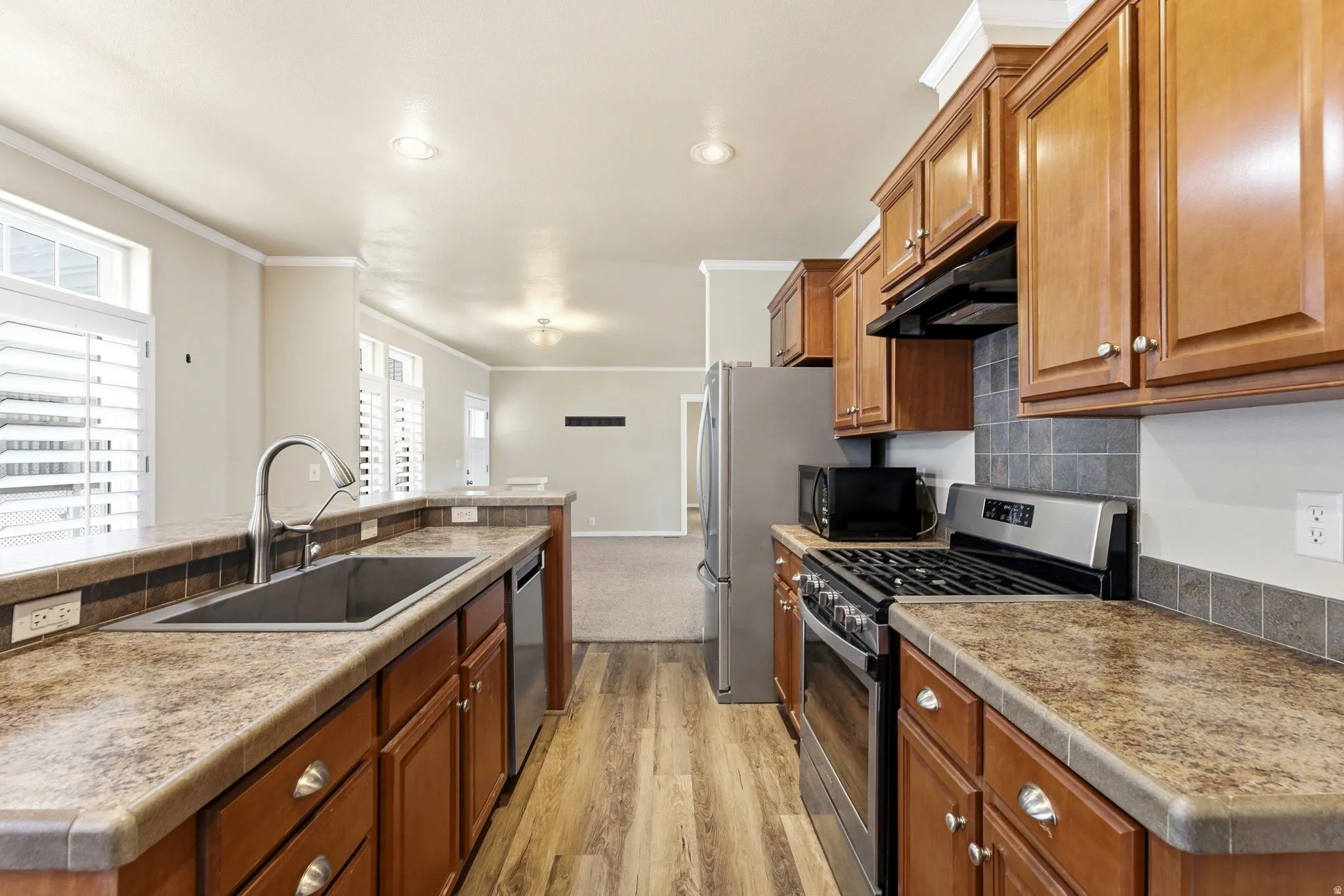 Kitchen featuring stainless steel appliances, wood finish cabinetry, light wood-type flooring, an island with sink, and ornamental molding