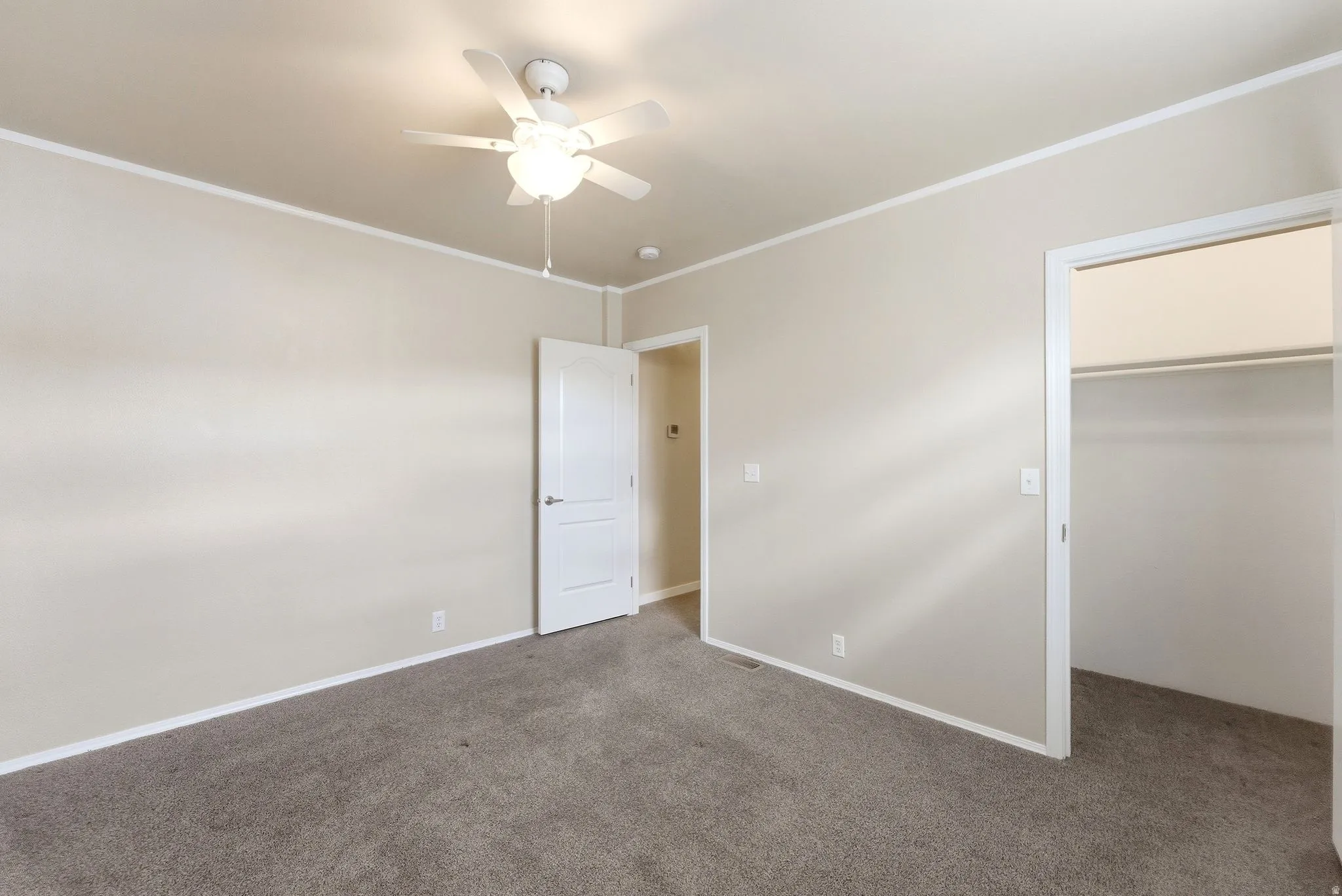 Unfurnished bedroom with a spacious closet, dark carpet, crown molding, and ceiling fan