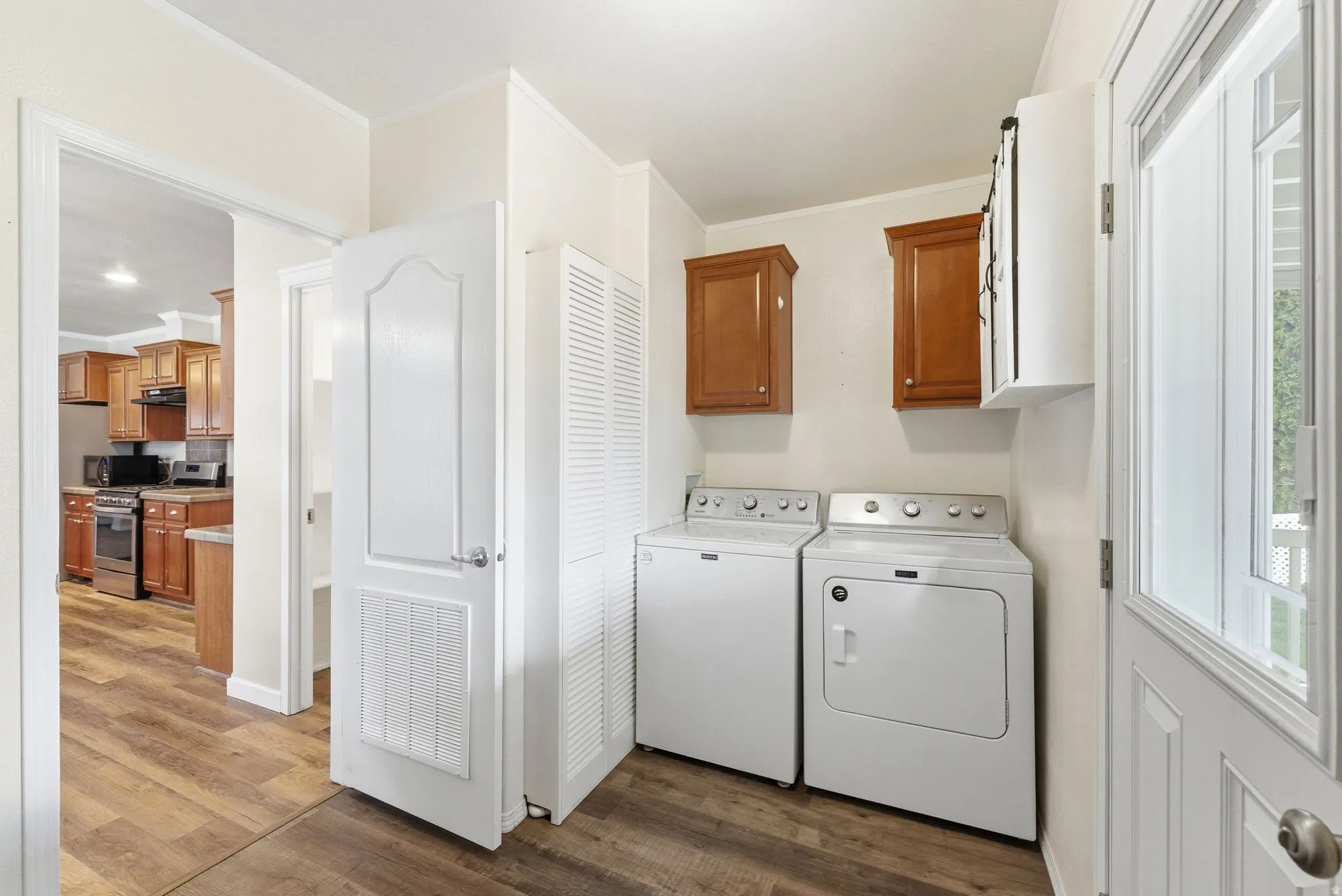 Laundry room with ornamental molding, dark wood-style floors, cabinet space, and washer and clothes dryer