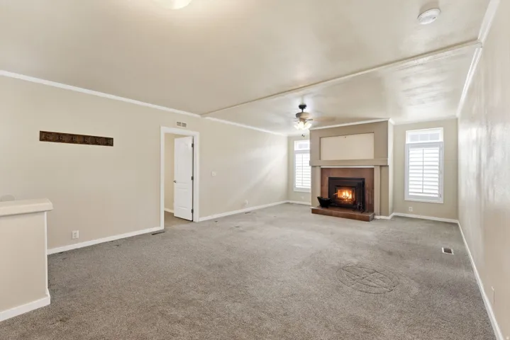 Unfurnished living room featuring a fireplace, ornamental molding, ceiling fan, and carpet flooring