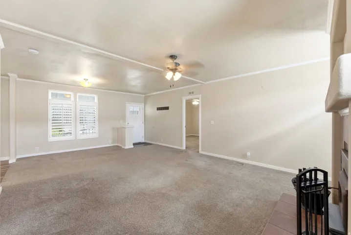 Unfurnished living room with ornamental molding, light carpet, a ceiling fan, and a fireplace