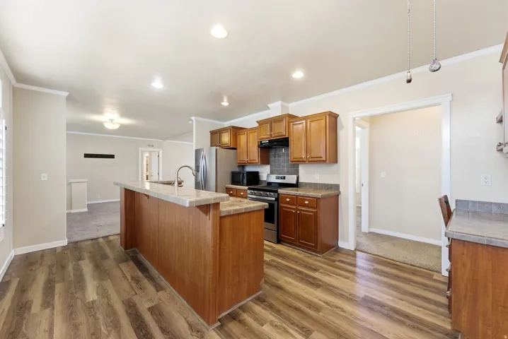 Kitchen featuring stainless steel appliances, wood finish cabinets, dark wood finished floors, a center island with sink, and ornamental molding