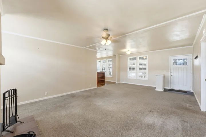 Unfurnished living room with light carpet, crown molding, and ceiling fan